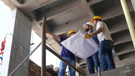 建筑工人、建筑师和工程师在建筑工地边谈边指着图纸