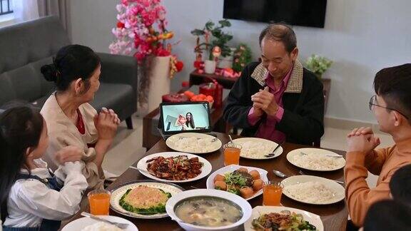 欢乐的亚洲家庭在家里吃团圆饭的时候通过数码平板电脑视频电话与亲戚们在网上欢度春节