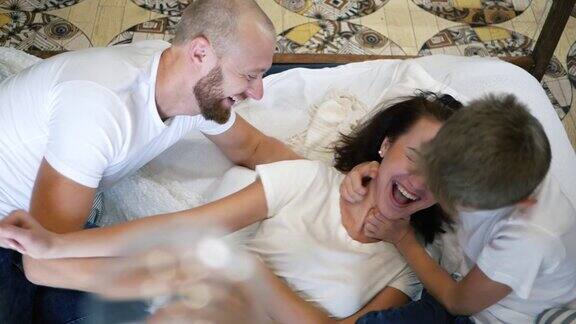 儿子和父亲在床上给母亲搔痒幸福的家庭一起在家里玩的时间