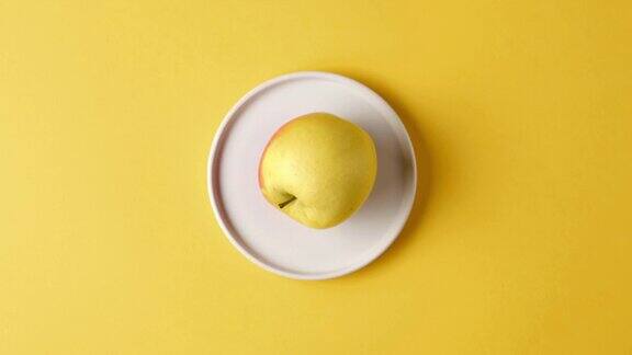红黄熟透的苹果在黄色背景的顶视图上绕着白色的盘子滚动停止运动视频