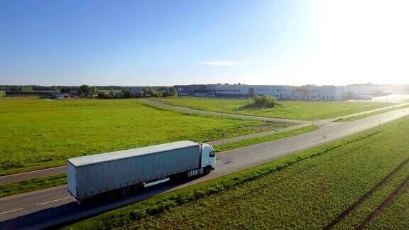 在高速公路上移动的白色半挂车的鸟瞰图在后台仓库和农村地区阳光普照