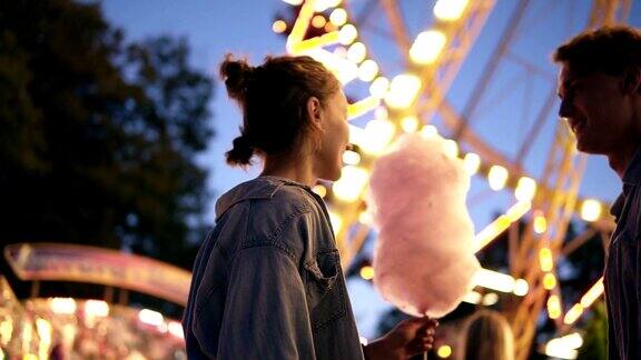 一对年轻情侣约会在游乐园见面男给她的女朋友带了一个棉花糖接吻在背景上亮一点低角度拍摄