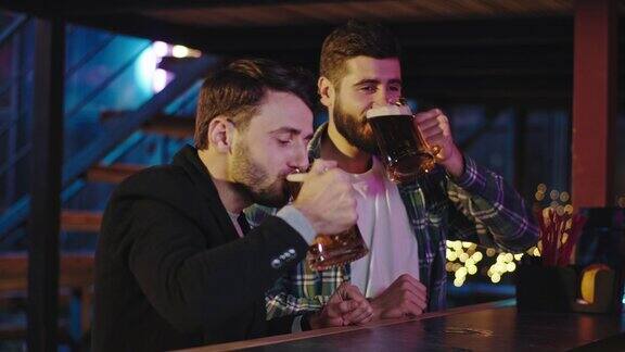 在一个啤酒酒吧里两个有魅力的家伙和一个好朋友喝着食物从一个大玻璃杯里拿着新鲜的啤酒他们享受着时光