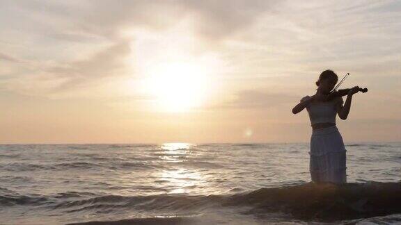 一个十几岁的女孩在日落的海滩上拉小提琴