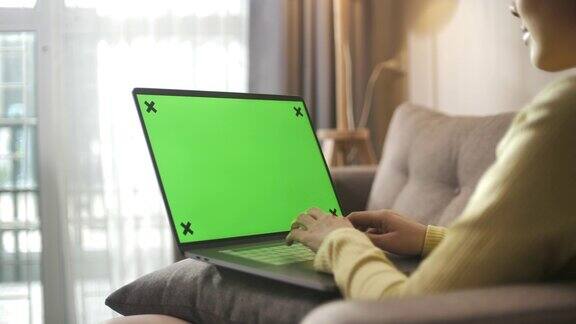 亚洲妇女坐在沙发上使用绿色屏幕的笔记本电脑