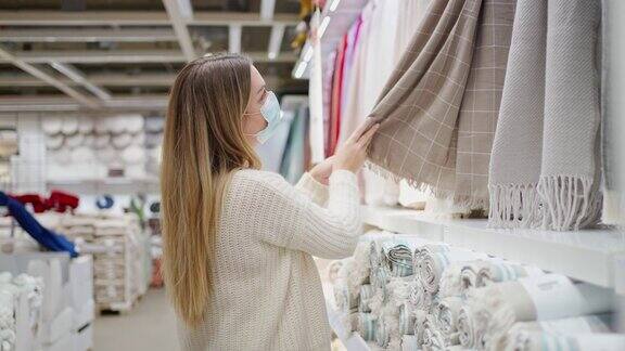 一名戴着防护口罩的妇女用手摩擦垂直挂着的毯子检查它们的质量柔软美丽多样的格子在一个家纺商店