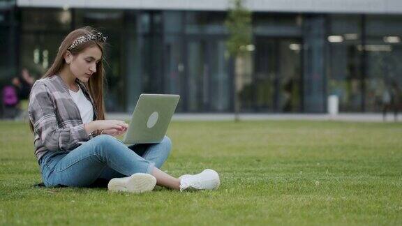 一位女大学生坐在草地上用笔记本电脑