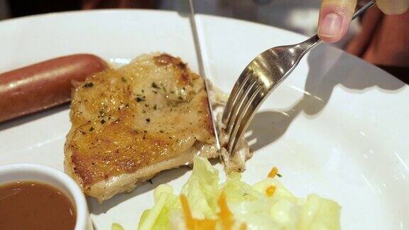 一个男性的手的特写用刀叉切和吃美味的沙拉鸡肉牛排