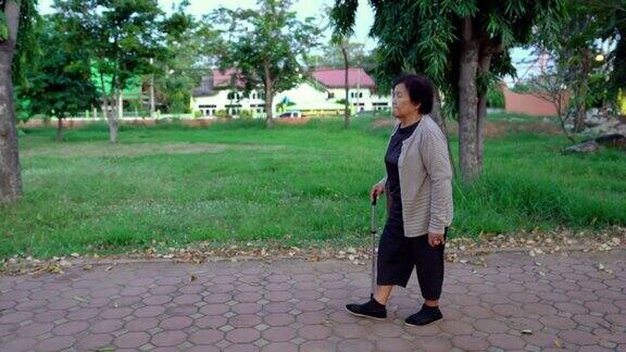 老妇人拄着拐杖在公园里散步
