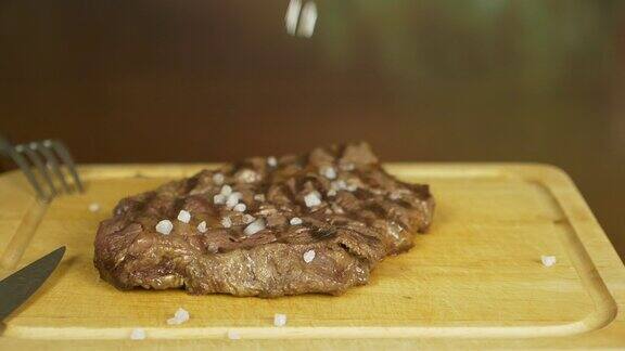 手盐牛排盐慢慢地落在肉上肉放在一块木板上