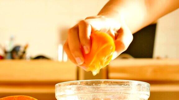 用手捏住半个橙子把橙汁挤到玻璃碗里