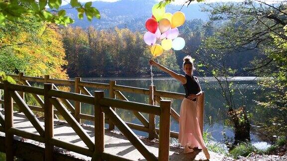 秋天美丽的芭蕾舞演员在湖边的木码头上与彩色气球一起跳舞(电影图片)