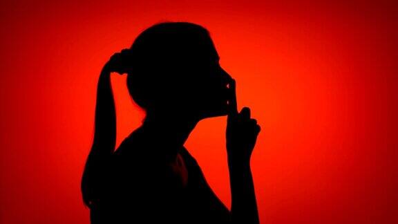 红色背景上年轻女子做沉默手势的剪影神秘和保密