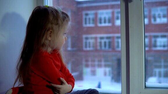可爱的小女孩坐在窗台上望着外面的雪景