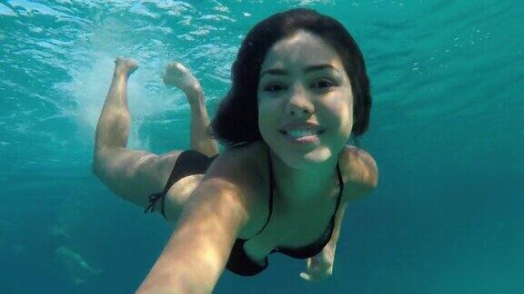 美丽的年轻女子在比基尼游泳水下和微笑的可穿戴相机