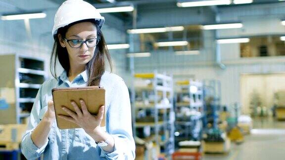 戴安全帽的女工业工程师在大工厂里使用平板电脑