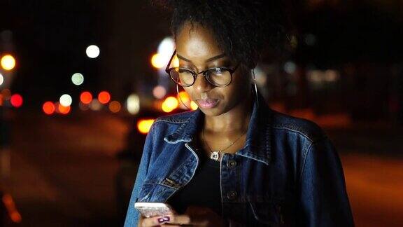 年轻黑人女性晚上在城市里用手机