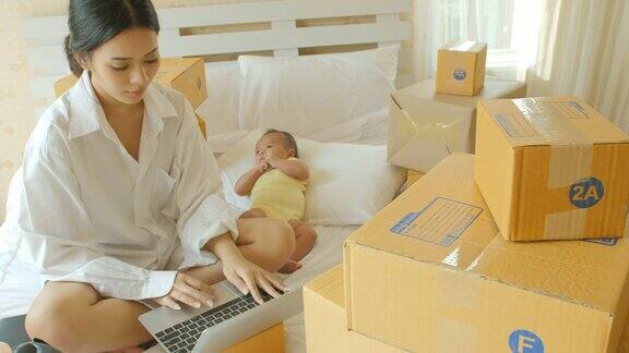 年轻的亚洲母亲和她的新生儿检查订单从笔记本电脑客户和在线交付准备装箱在卧室