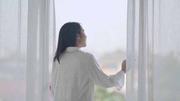 年轻女子早晨拉开白色的窗帘望向窗外