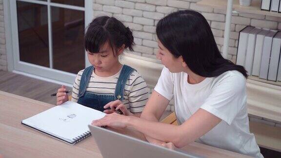 母亲一边帮女儿做美术作业一边用笔记本电脑进行在线教育和在家工作