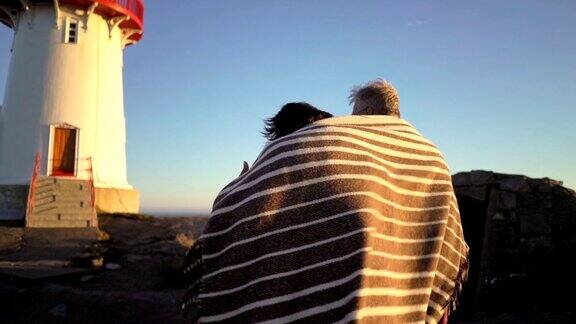 一对成熟的夫妇在日落时分与一座古老的灯塔漫步在海边