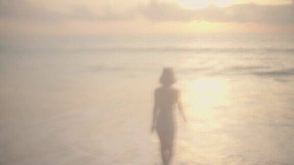 快乐的女孩穿着泳衣在金色日落的背景附近的大海