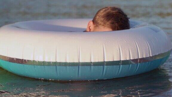 快乐的男孩在海里游泳躲在一个充气的甜甜圈后面