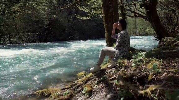 一个年轻女子坐在湍急的河流附近的岸边她看着水
