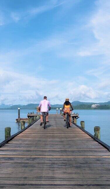 一对夫妇骑着自行车在泰国一个热带岛屿的木码头上