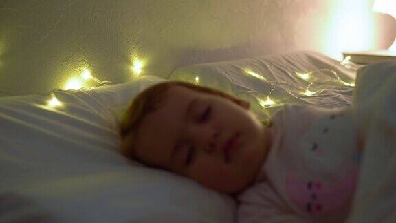 1-2岁的小女孩穿着粉红色的睡衣睡在白色的床上孩子晚上有放松的休息时间枕头上的花环童年、圣诞节、亲子观念