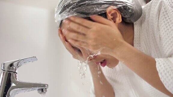 亚洲妇女在清晨在浴室用干净的水清洁脸部
