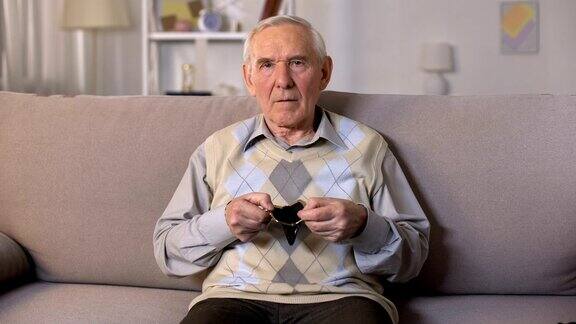 悲伤的老人坐在沙发上在镜头前展示着空空的钱包贫穷