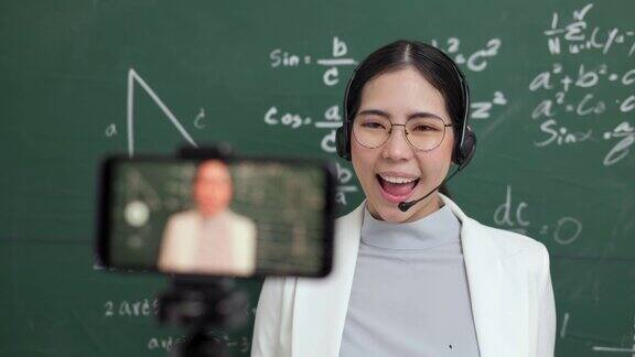 年轻的亚洲女教师站在摄像机和学生视频会议女教师在课堂上通过智能手机在线课程直播培训数学