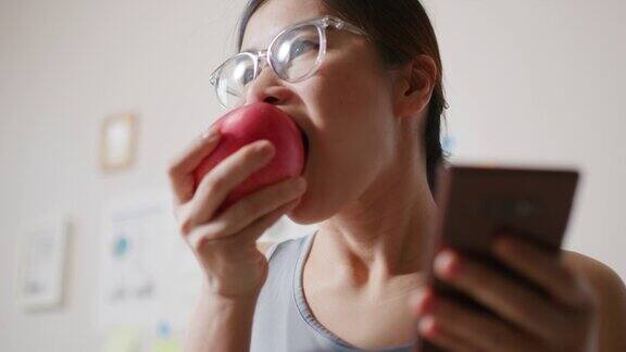 年轻健康的女性一边吃苹果一边用手机
