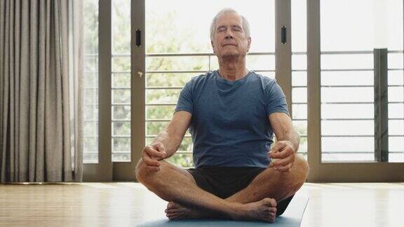 一位老人坐在家里做瑜伽一位长者坐在席子上冥想