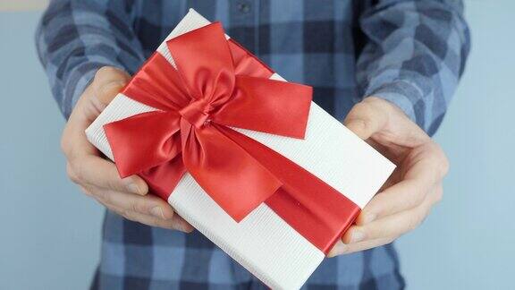 男子拿着并展示了系着红色蝴蝶结的白色礼品盒走向镜头特写男性手中的情人节礼物手正在赠送礼盒