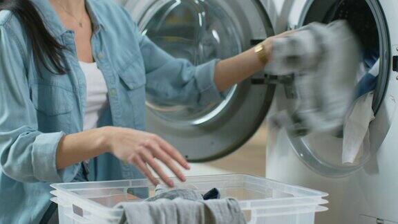 一个美丽的年轻女人在家常的衣服坐在洗衣机前的特写她把脏衣服装在洗衣机里明亮宽敞的客厅现代的室内设计