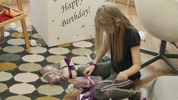 一个可爱的女孩在气球的背景下打开她的生日礼物