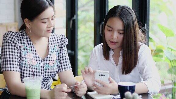 两个亚洲女人在咖啡馆喝咖啡用智能手机在网上购物