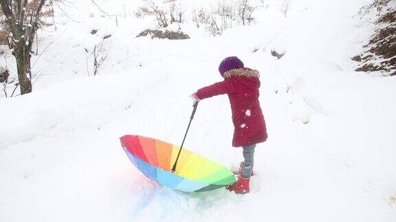 小女孩在雪地里捻着五颜六色的伞