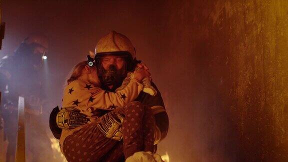 勇敢的消防员抱着一个被救下的女孩走下燃烧的大楼的楼梯