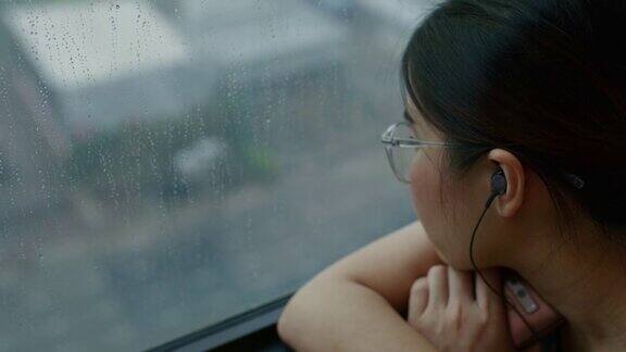 忧伤的女人坐在窗边看雨听着音乐