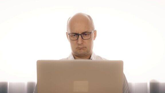戴眼镜的悲伤的男人用笔记本工作因为疲劳而揉眼睛