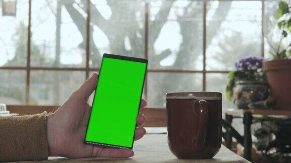 一个男人的手拿着一个绿色屏幕模型的手机喝着咖啡版本2