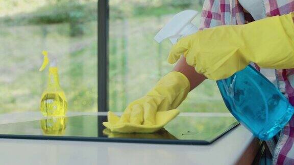 一名戴黄色橡胶手套的妇女正在用去脂喷雾和抹布清洁厨房的炊具面板