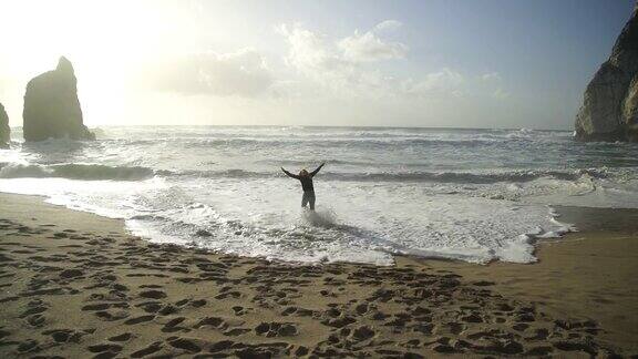 日落时分一个金发女人朝着海滩上的海浪走去