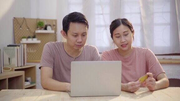 年轻的亚洲夫妇使用笔记本电脑和信用卡在家里网上购物