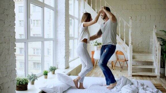 年轻美丽和相爱的夫妇跳舞和亲吻在床上在家里的早晨