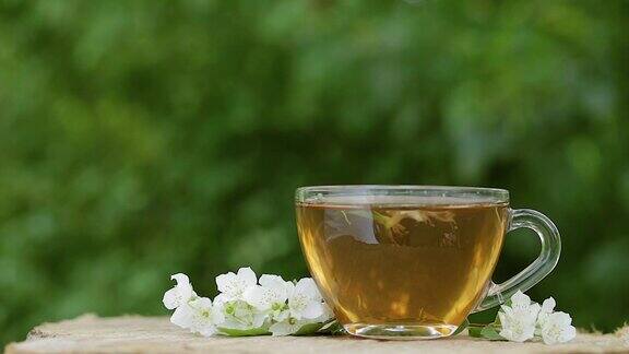 一杯茉莉花绿茶茉莉花茶和茉莉花的木制背景茉莉花和叶子慢动作将茶倒入杯中用茶匙搅拌