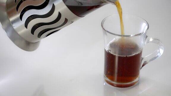 用法式滤茶器将茶倒入一个透明的杯子中在白色的背景上